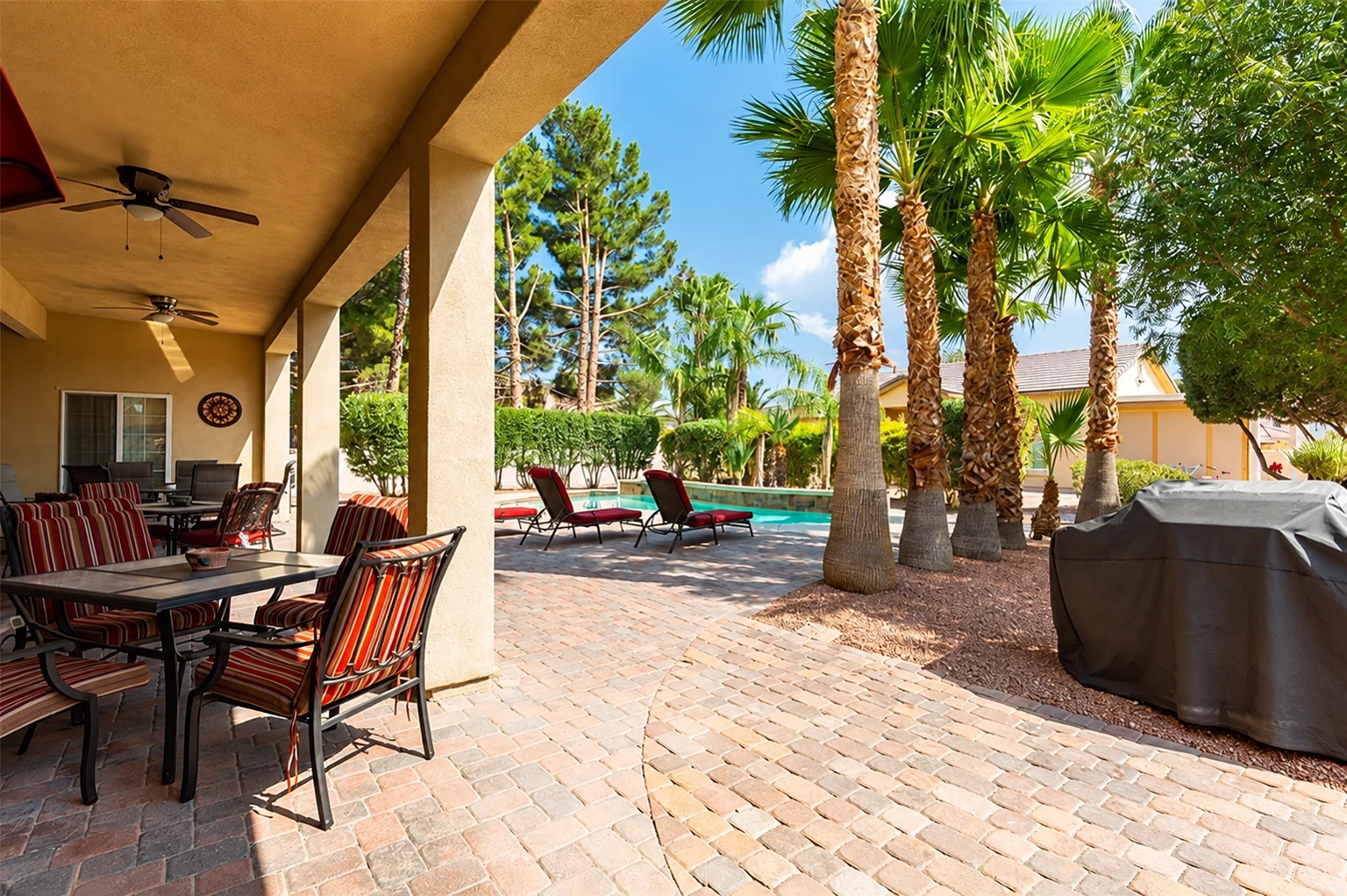 Covered patio at Rise with outdoor tables and chairs beside the pool and palm trees.